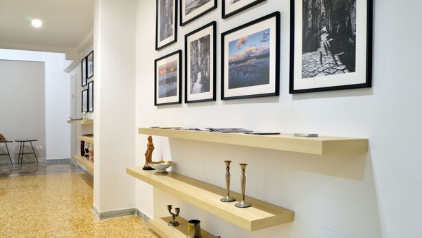 A hallway with a series of framed pictures on the wall, wooden shelves with decorative items, and a tiled floor. - B&B La Locanda dell'Arte Museo (Naples)