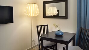 A hotel room with a dark wooden table, a blue vase with white flowers, a standing lamp, a framed mirror, and a flat-screen TV mounted on the wall. - B&B La Locanda dell'Arte Museo (Naples)