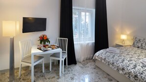 A hotel room with a bed, a desk with a chair, a TV mounted on the wall, and a window with curtains. - B&B La Locanda dell'Arte Museo (Naples)