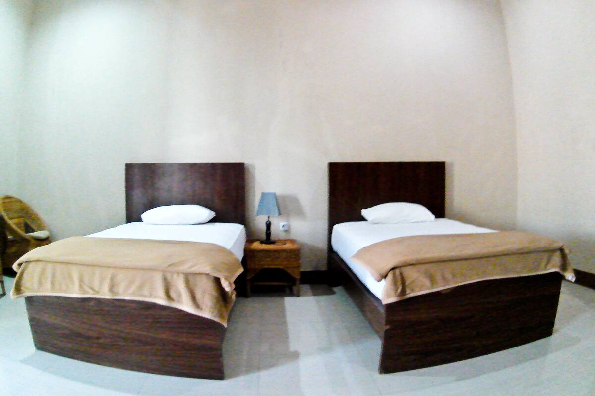 A hotel room with two single beds, each with a wooden headboard, a nightstand with a lamp, and a chair.