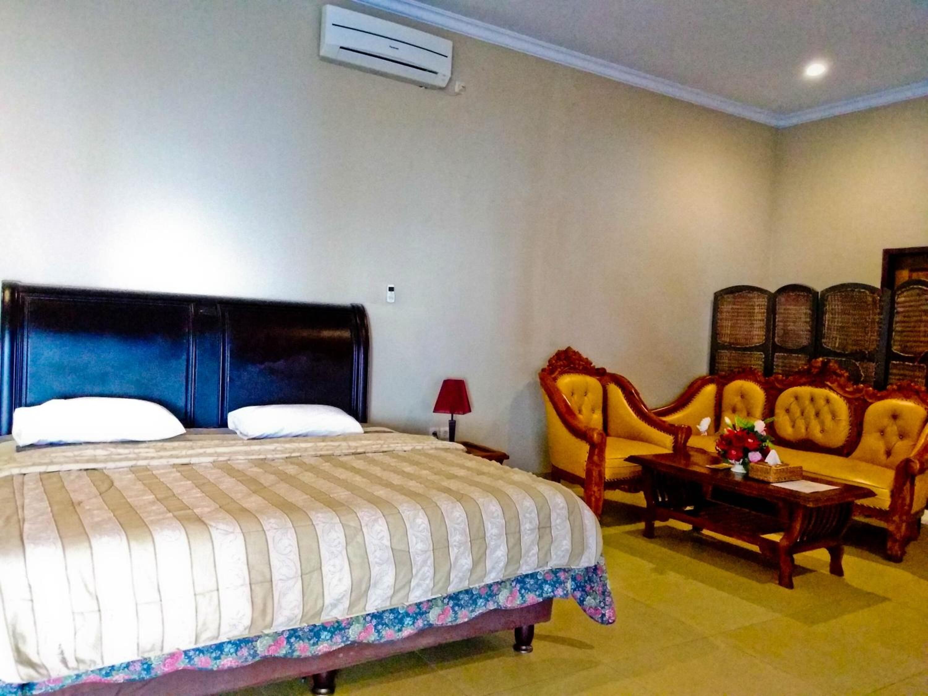 A hotel room with a large bed, a sofa, a small table, and a decorative chair.