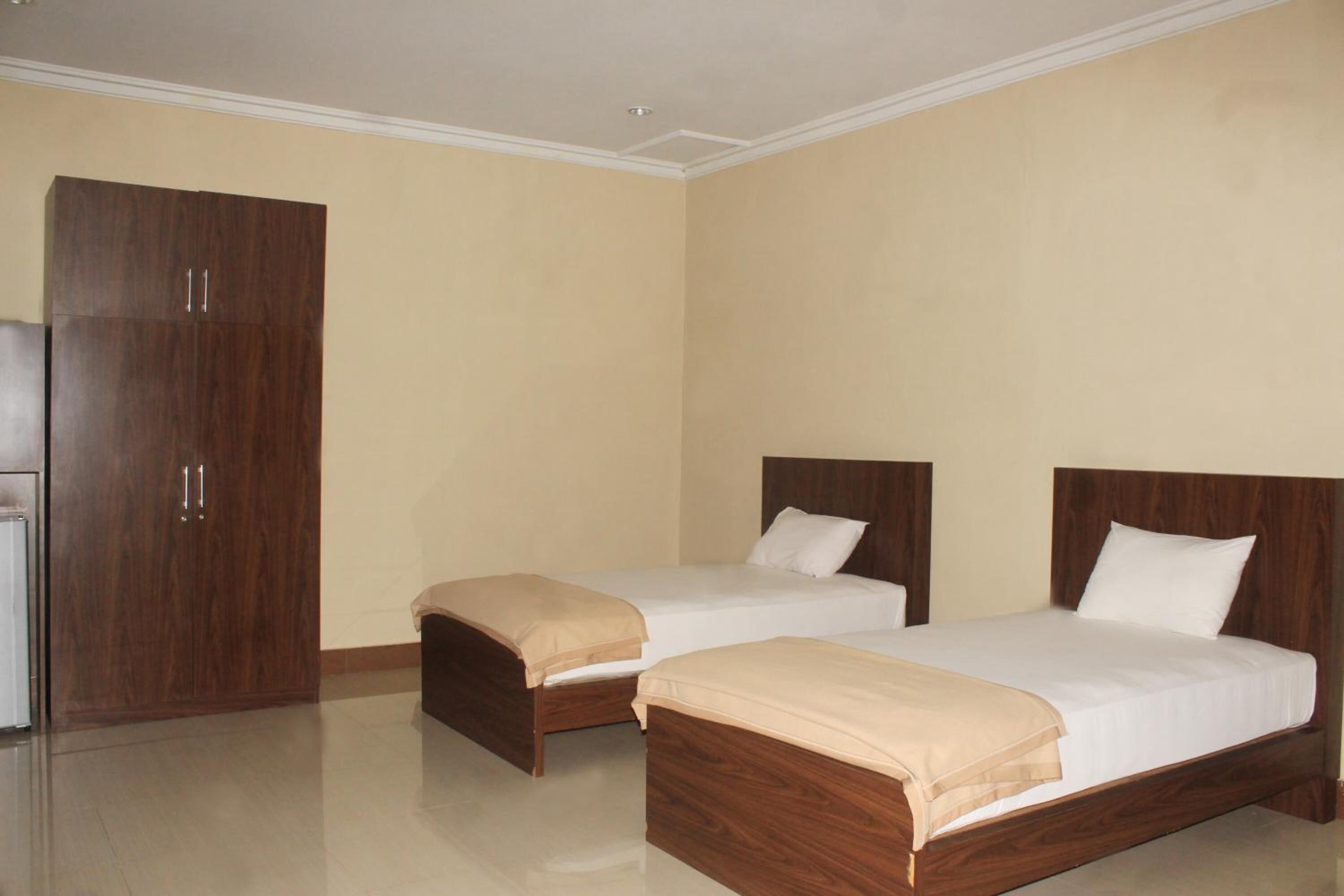 Quarto de hotel com duas camas, um guarda-roupa e uma pequena cozinha equipada.