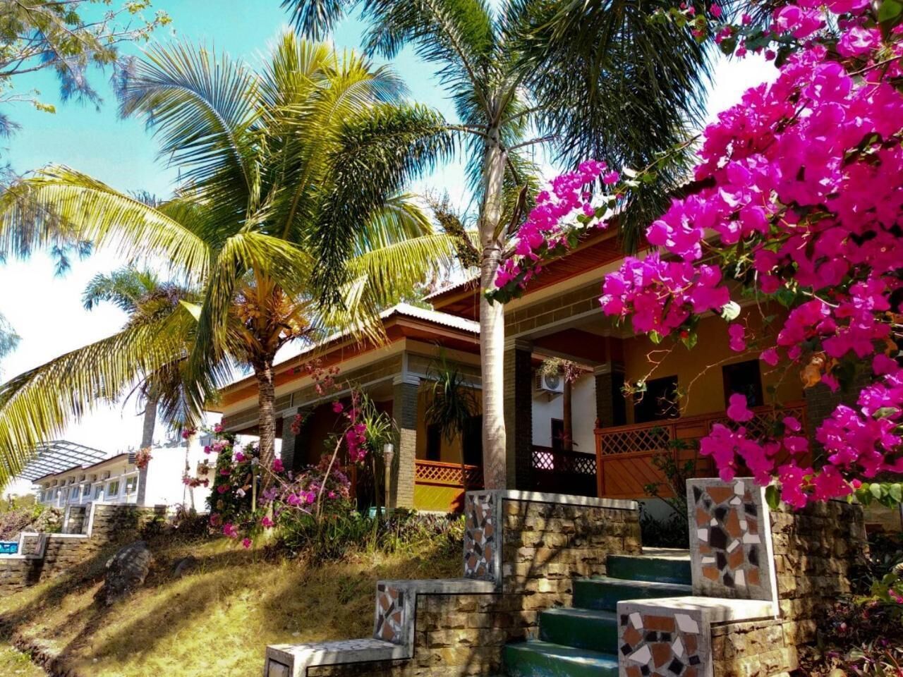 A tropical resort with a two-story building, palm trees, and vibrant pink bougainvillea flowers.