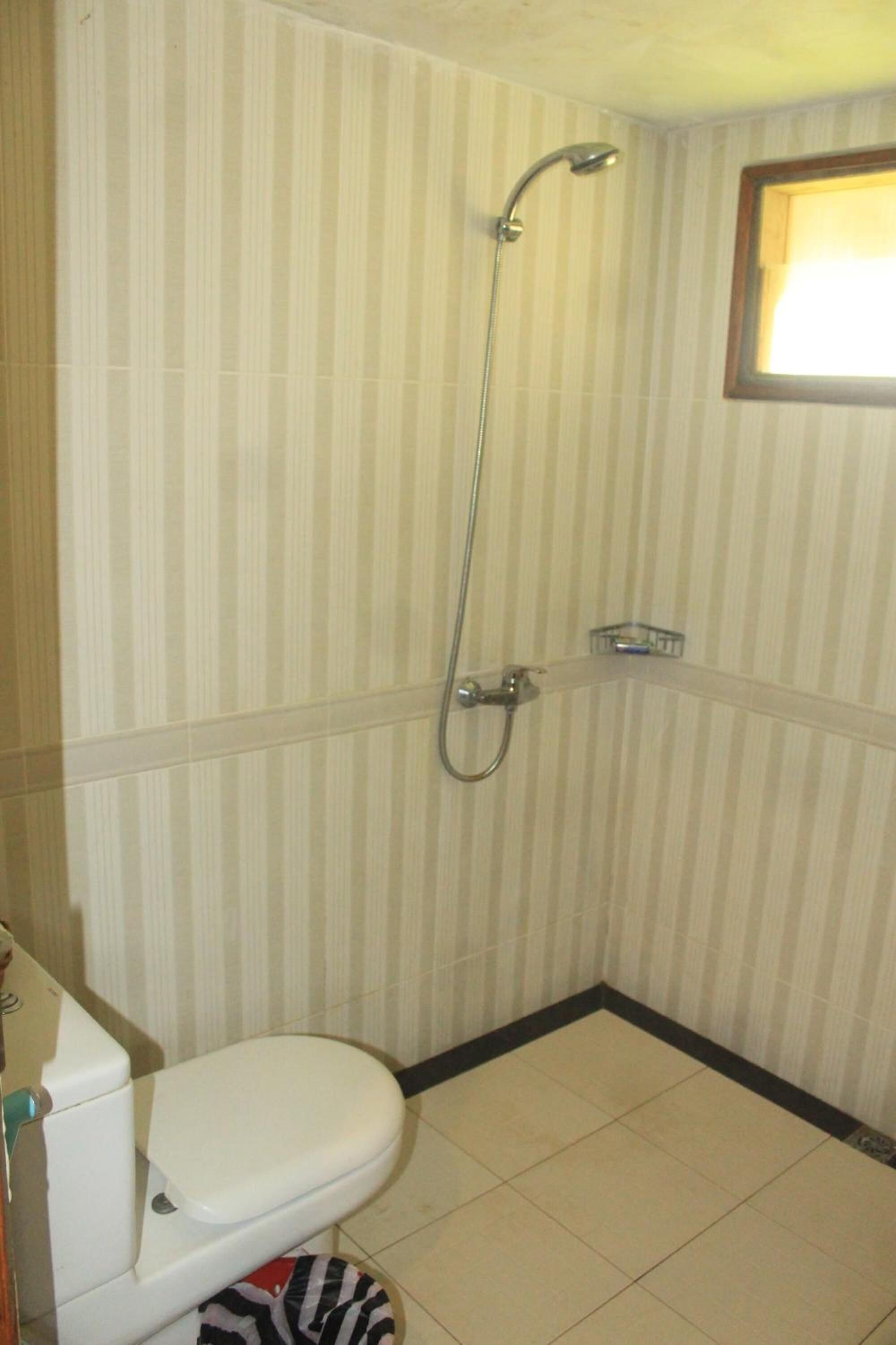 A small bathroom with a toilet, a shower, and a window.