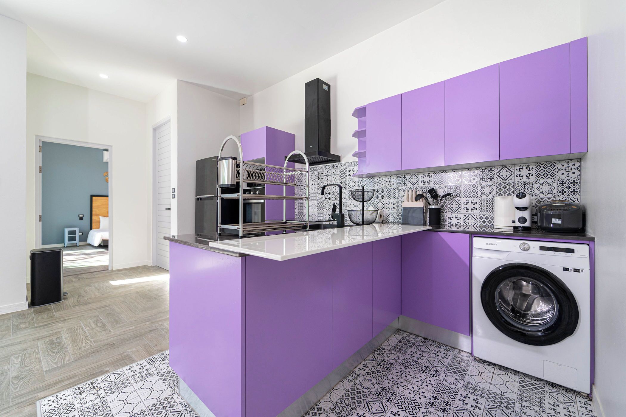 A compact kitchen with purple cabinets, a washing machine, and a patterned backsplash.