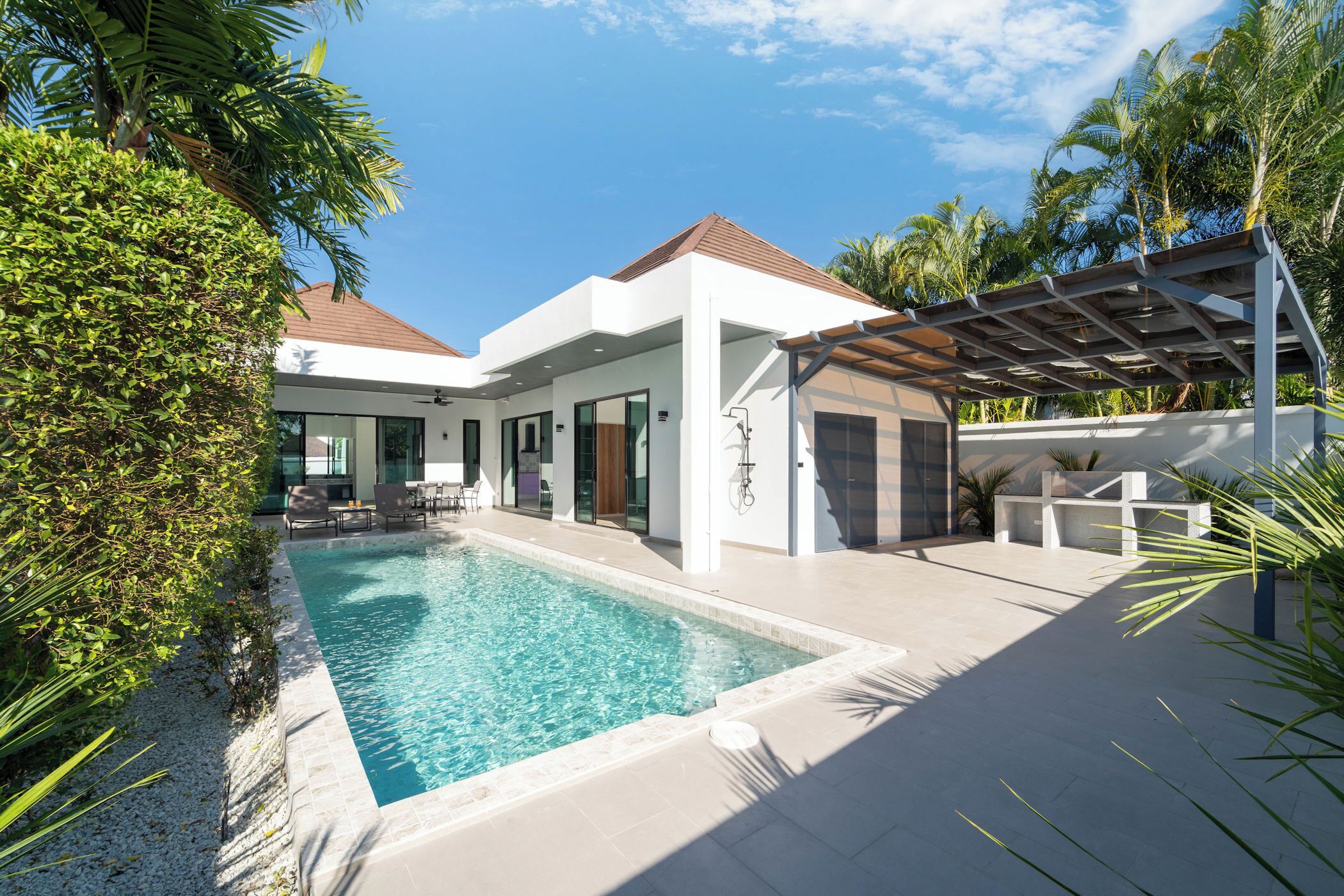 A modern house with a swimming pool, surrounded by tropical plants and a pergola.