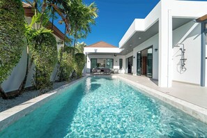Un espace piscine moderne avec une eau d’un bleu limpide, entouré de murs blancs et de plantes tropicales.