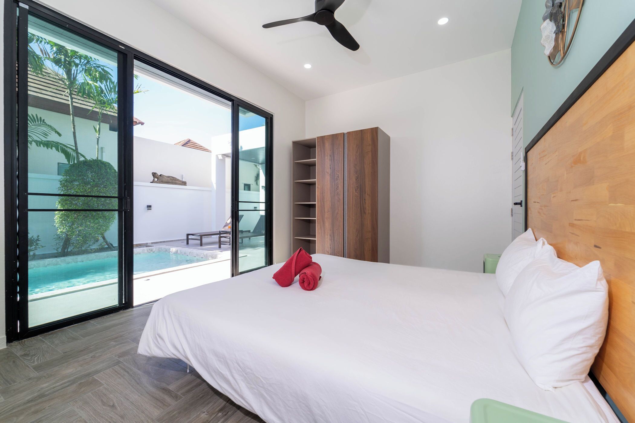Un dormitorio moderno con una cama grande, cabecera de madera y puerta corrediza de vidrio que da a una zona de piscina.