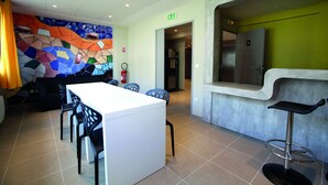 A modern hotel lobby with a white reception desk, blue chairs, a colorful mosaic wall, and a bar area with a stainless steel refrigerator. - Residence Les Portes d'Espagne (Perpignan)