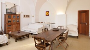 A spacious living area with a wooden dining table, white sofas, and a wooden cabinet. - Masseria Autigne (Otranto)