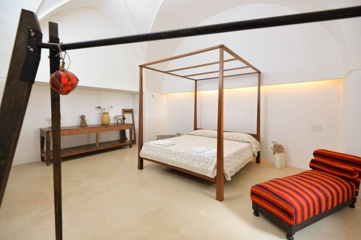 A bedroom with a four-poster bed, a wooden bench, and a red-striped sofa.