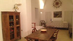 A cozy room with a wooden dining table, a cabinet with glass doors, a bed with patterned bedding, and a wall-mounted decorative piece. - Masseria Autigne (Otranto)