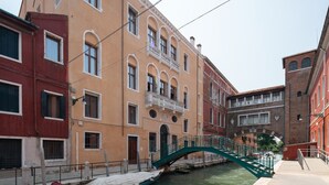 Un canal surmonté d’un pont vert, des bâtiments dotés d’arcs en plein cintre et un ciel dégagé.