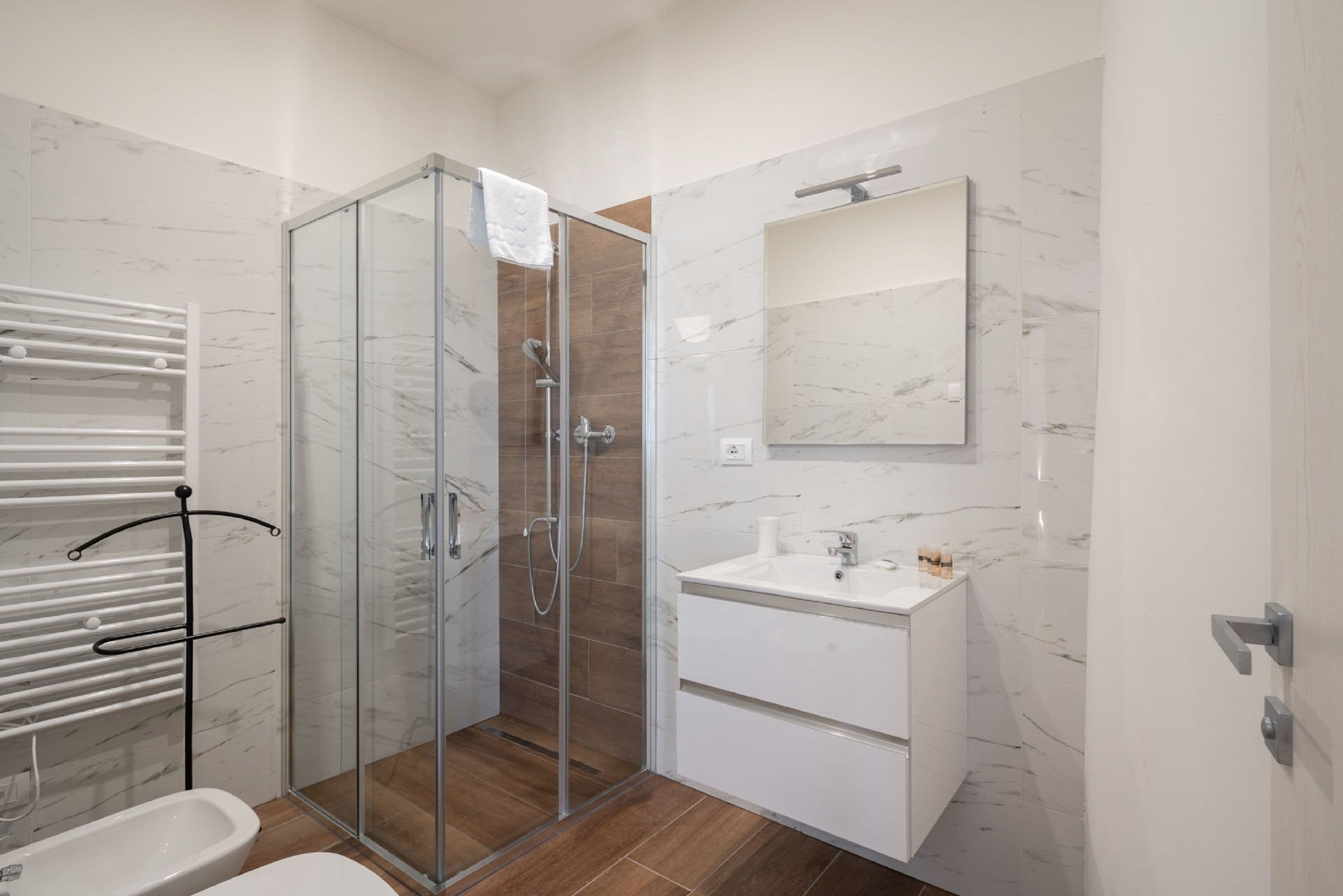 A modern bathroom with a glass shower enclosure, a white sink, and a marble-tiled wall.