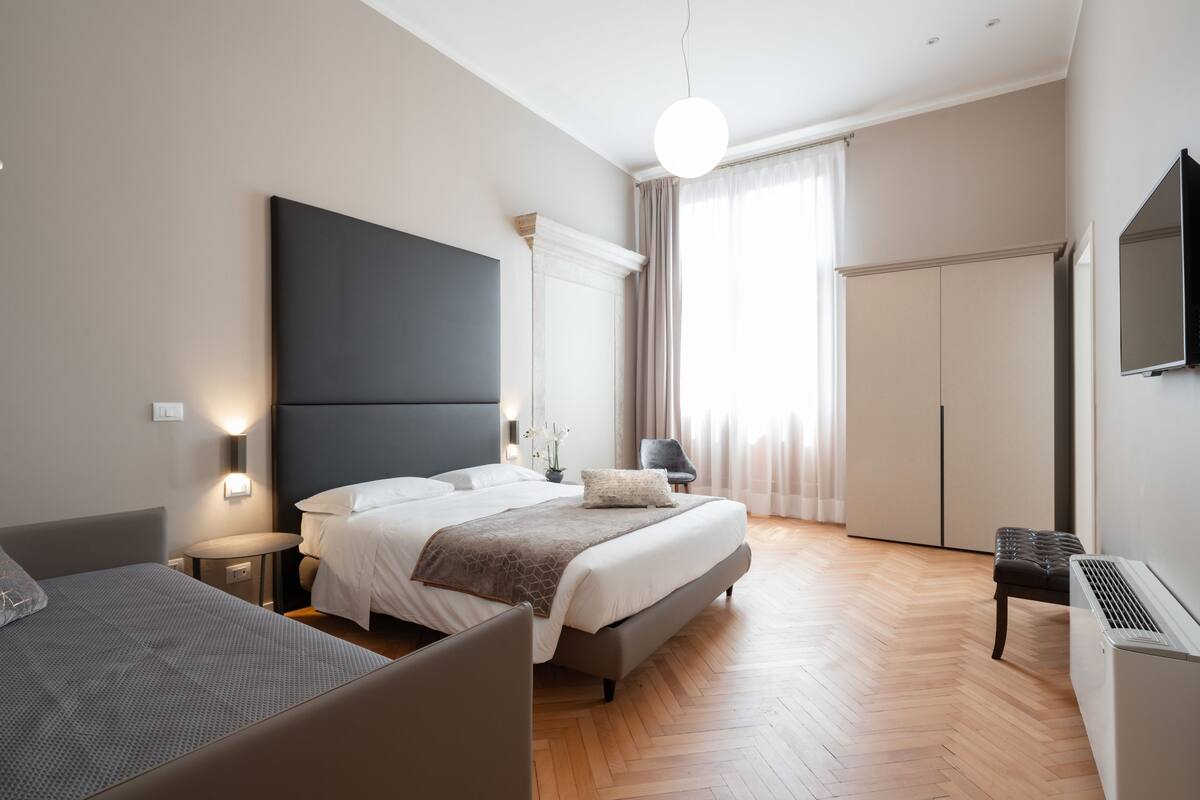 A modern bedroom with a large bed, bedside tables, a TV, and a wardrobe.
