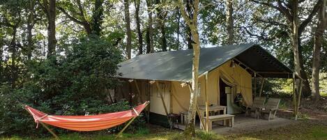 A tented accommodation with a hammock, surrounded by trees.