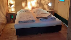 Um quarto tipo tenda, com uma cama, duas luminárias de cabeceira e uma pequena janela.