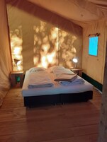 Um quarto tipo tenda, com uma cama, duas luminárias de cabeceira e uma pequena janela.