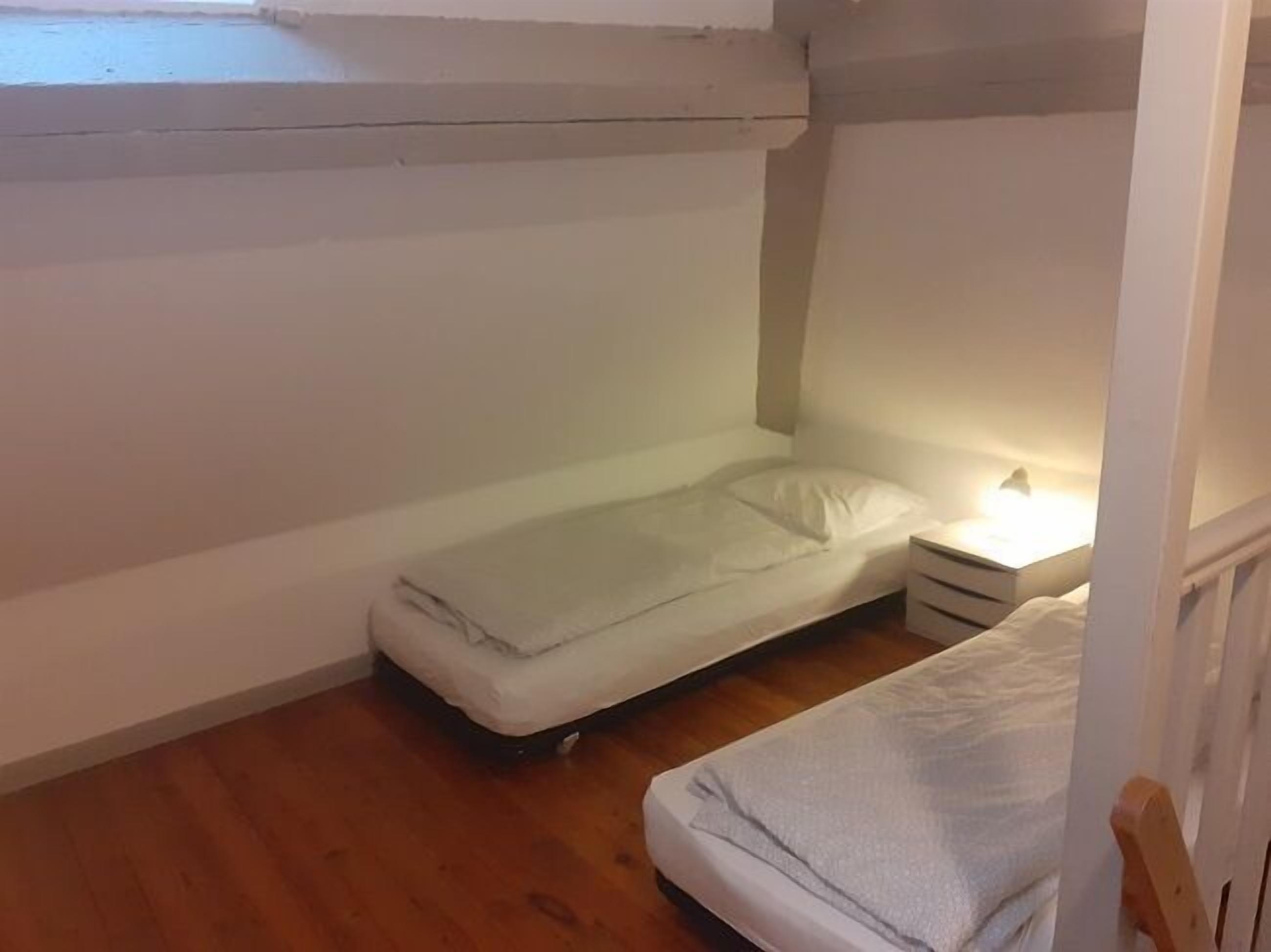 Une petite chambre avec un lit simple, un plancher en bois, une table de chevet et une fenêtre.