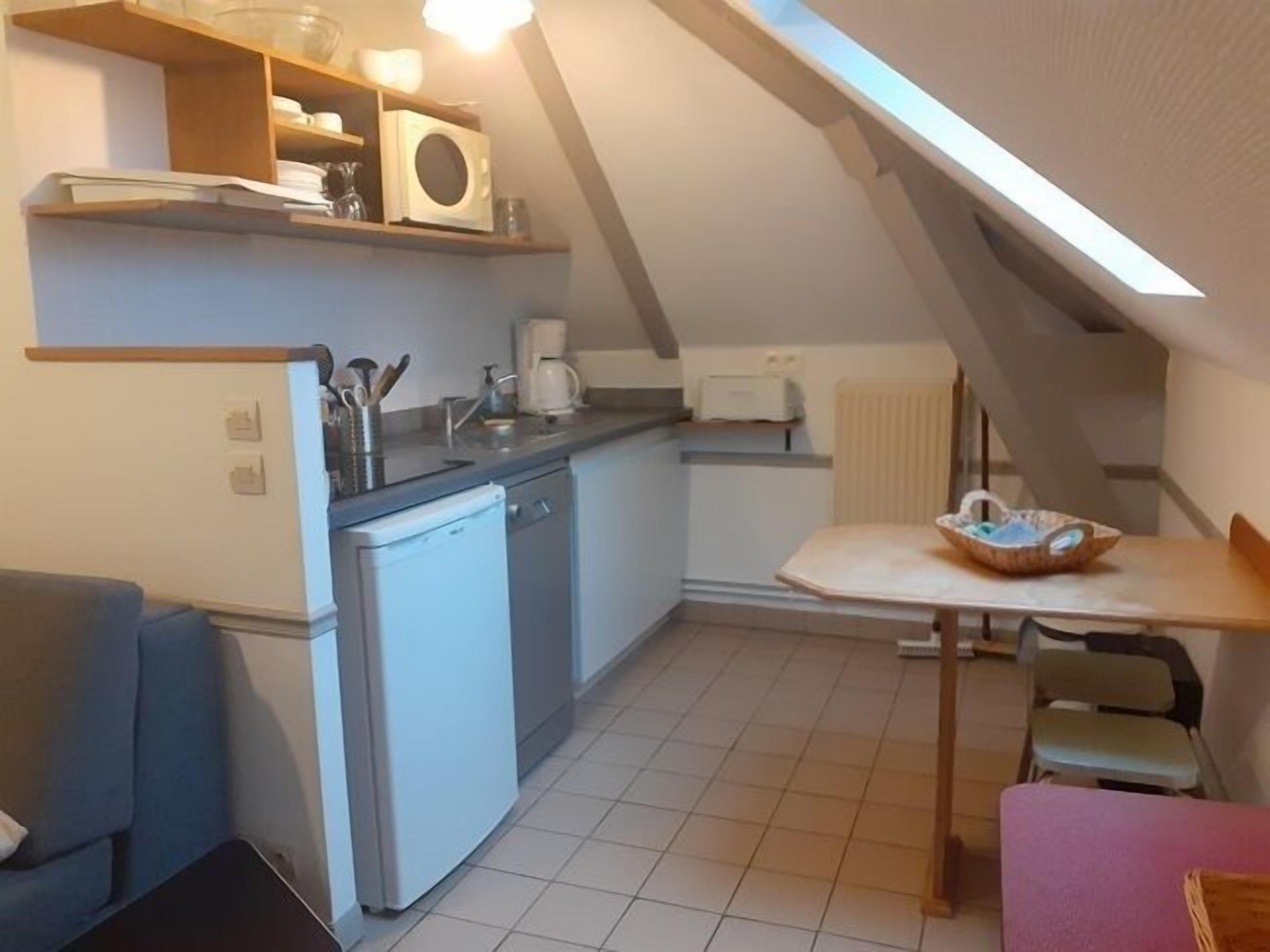 Een kleine keuken met een vaatwasser, een koffiezetapparaat en een magnetron op een houten plank.