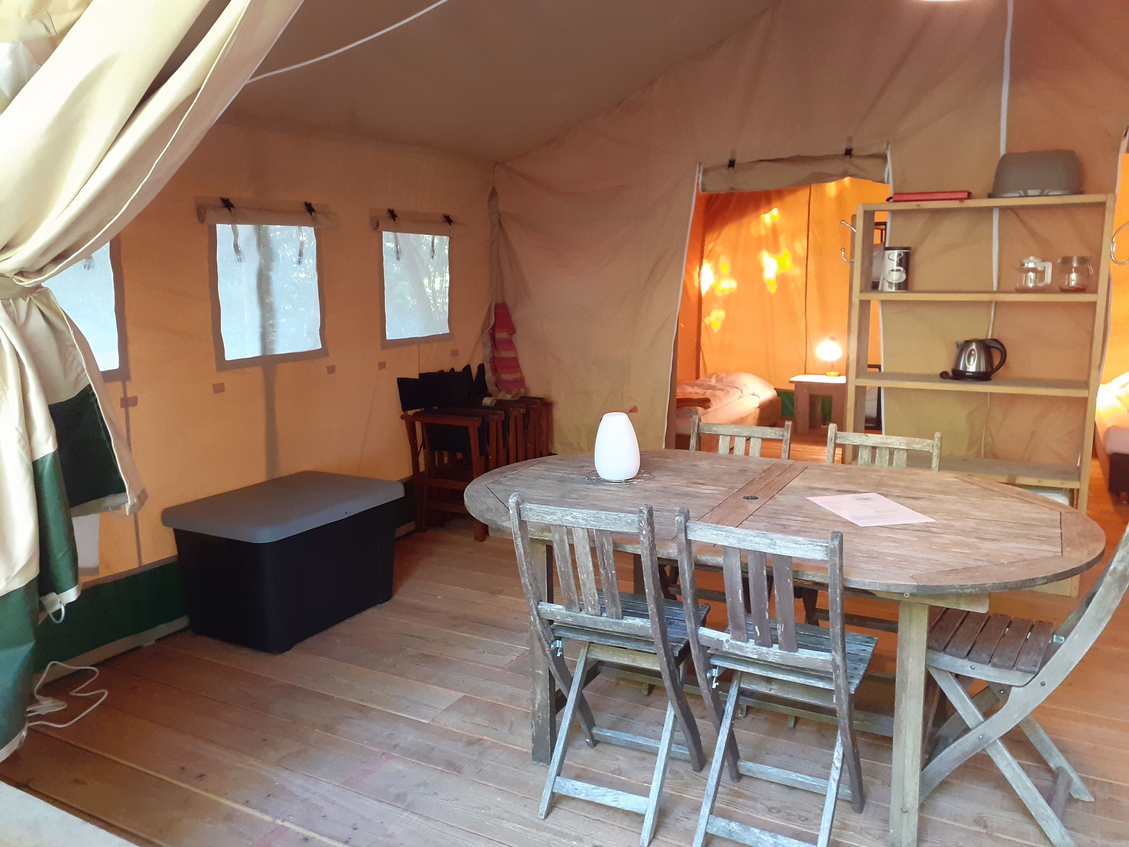 A tent with a wooden table and chairs, a bench, and a shelf with kitchen items.