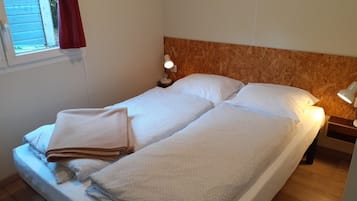 A single bed with a wooden headboard, two pillows, a bedside lamp, and a window with a red curtain.