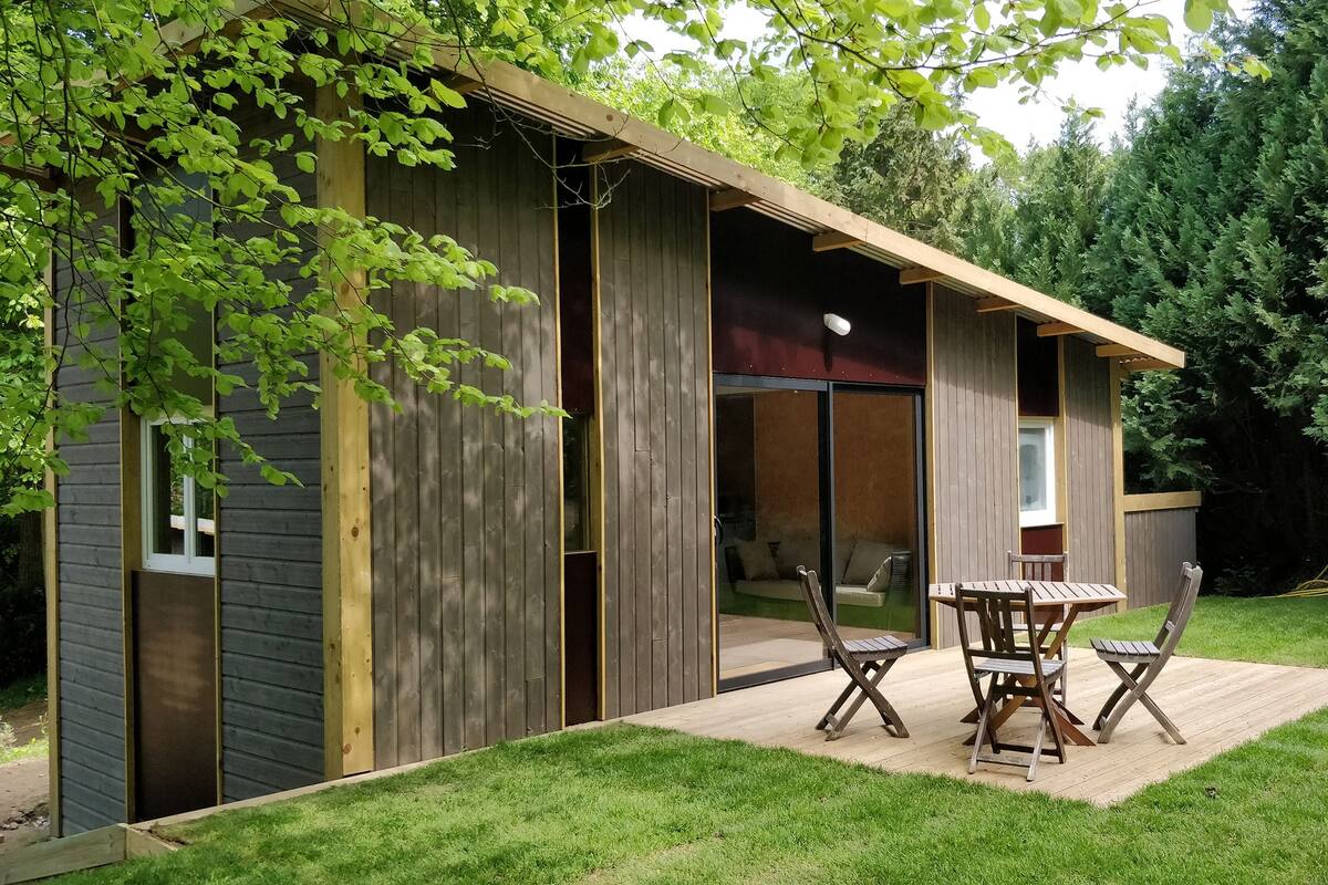Una cabaña de madera con un patio, un ventanal corredero y una pequeña mesa con sillas.