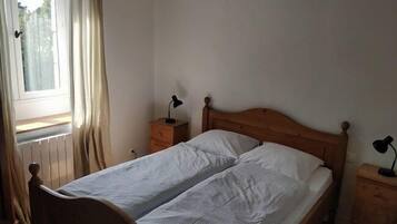 A simple, unadorned bedroom with a wooden bed, two bedside tables, and a window with curtains.