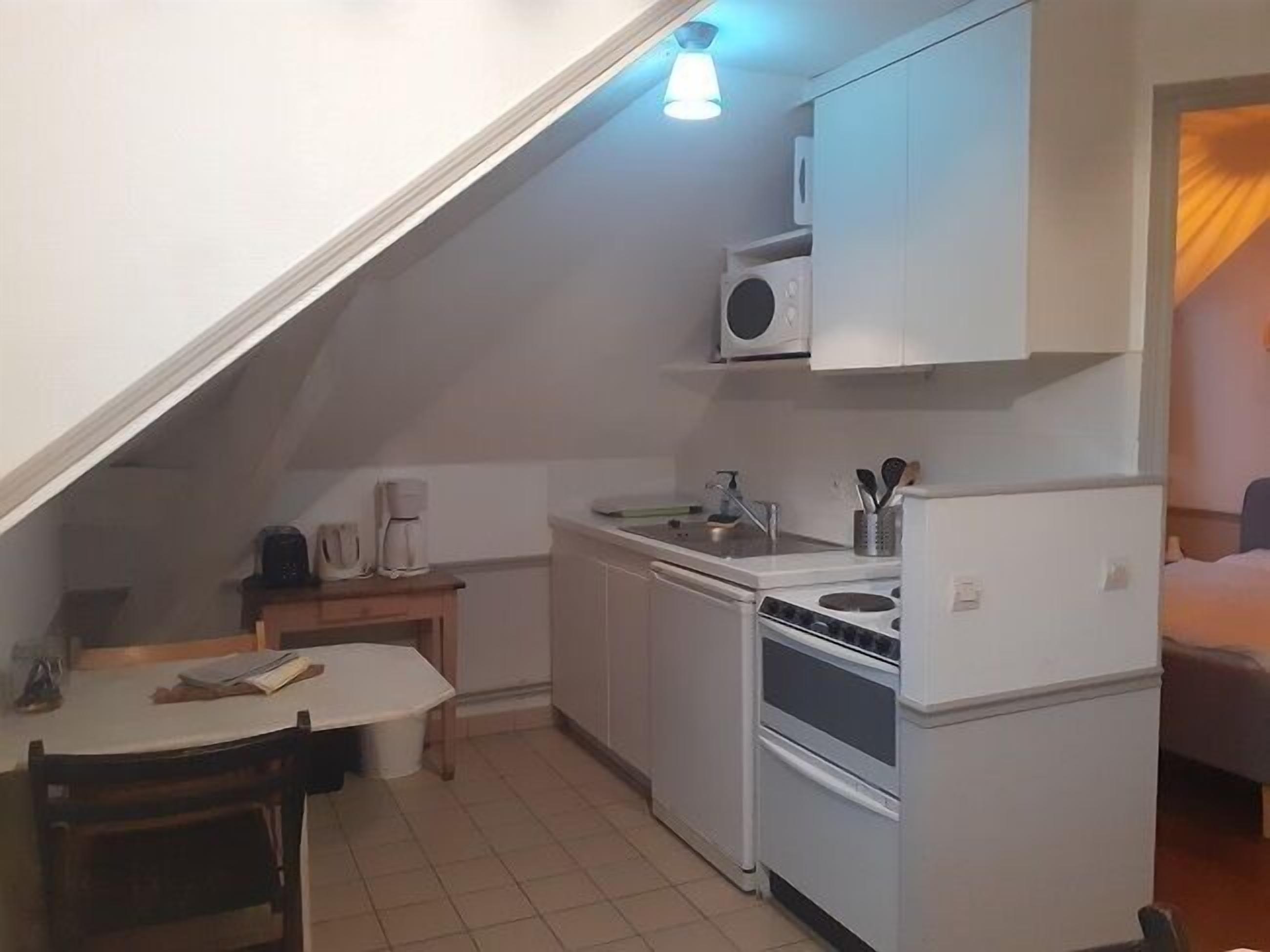 A compact kitchen with white cabinets, a stove, a sink, and a coffee maker.