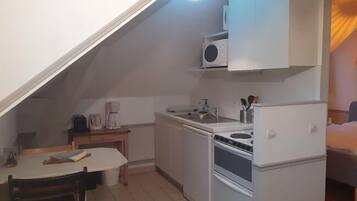 A compact kitchen with white cabinets, a stove, a sink, and a coffee maker.