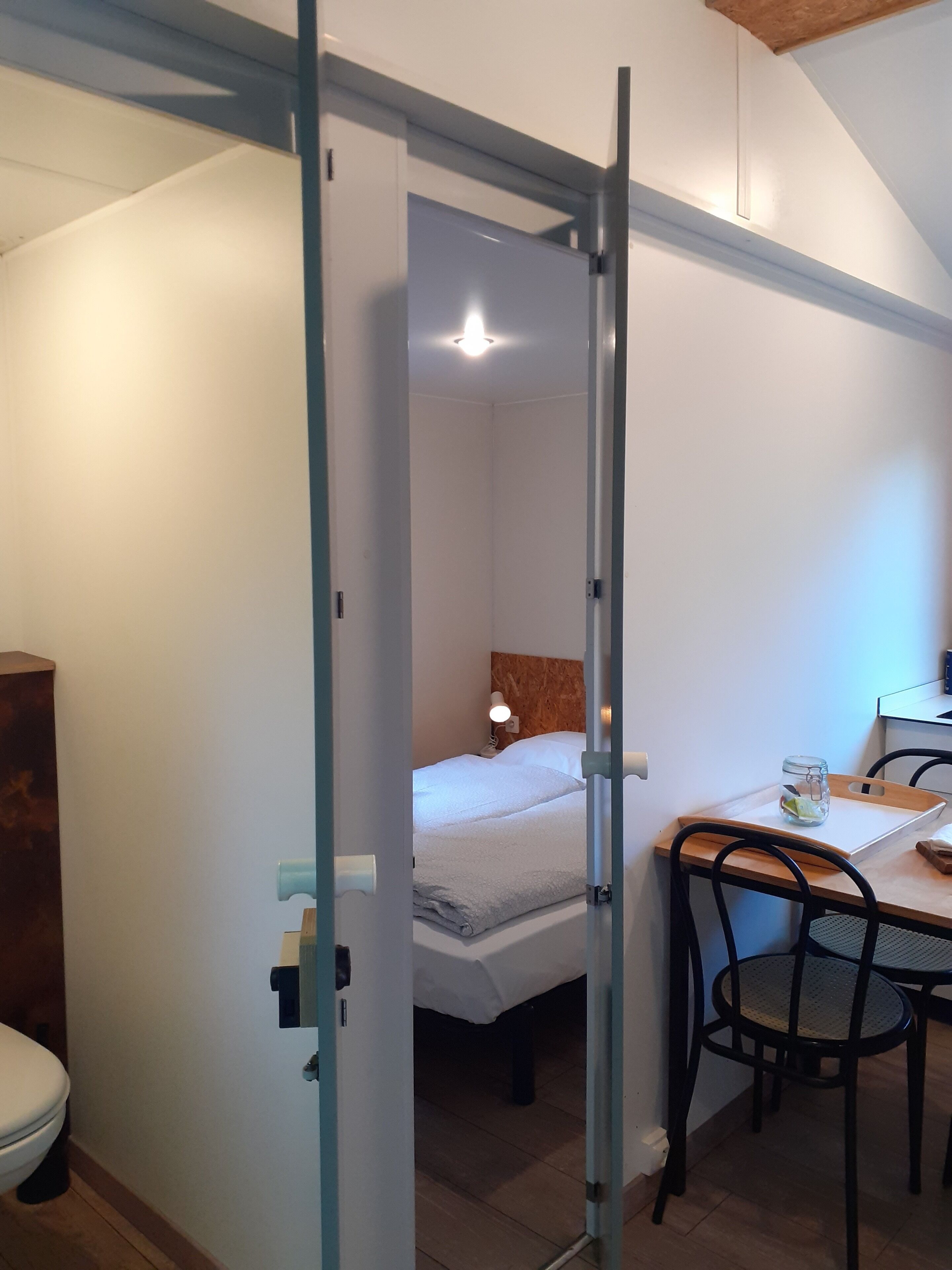 A bedroom with a bed, bedside table, and a desk with chairs.