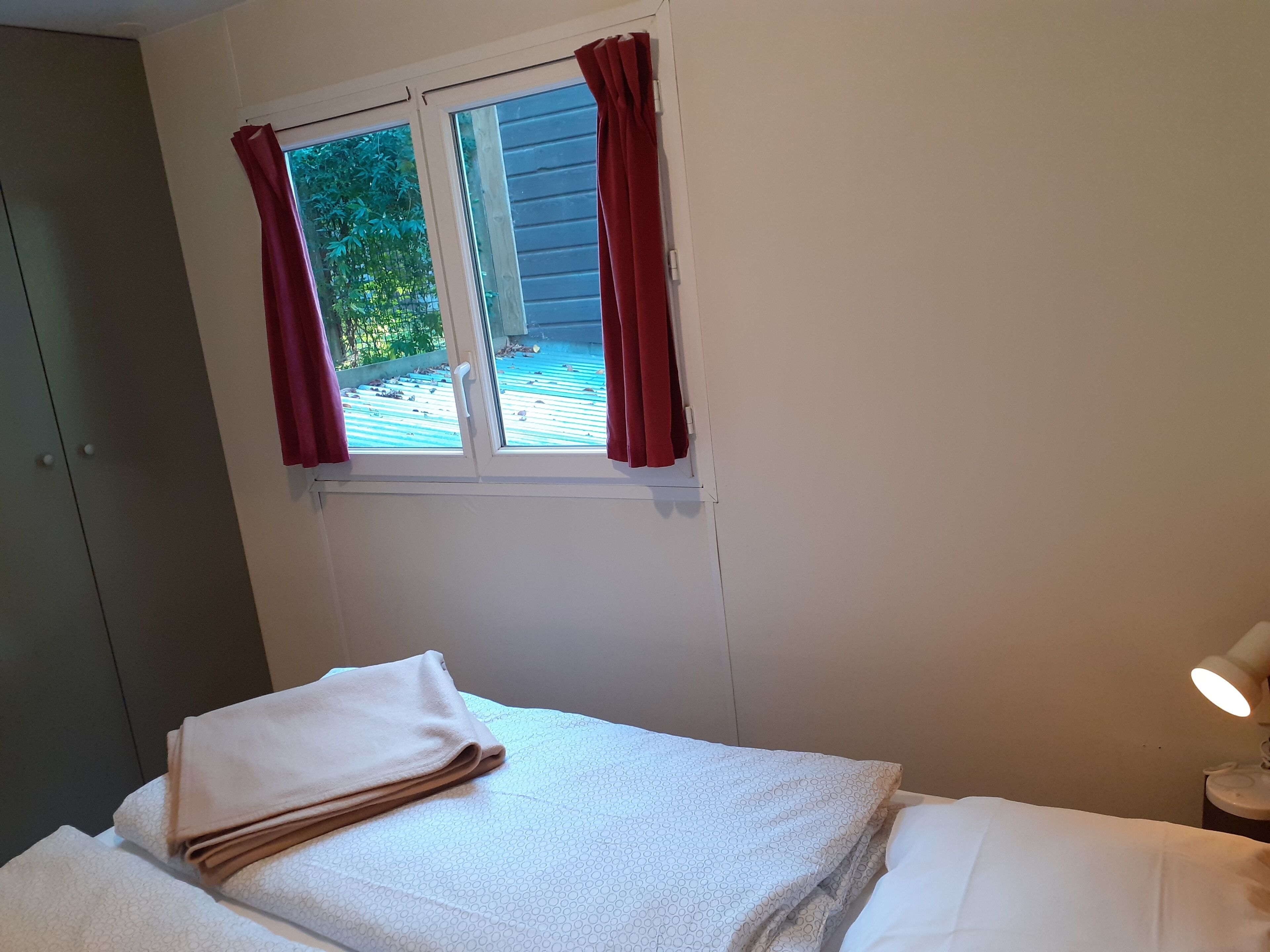 Una habitación con cama, ventana con cortinas, lámpara de noche y vista al exterior.
