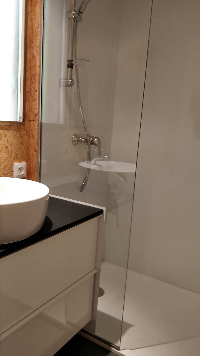 Une salle de bain moderne avec un lavabo blanc, une douche en verre et un comptoir noir.