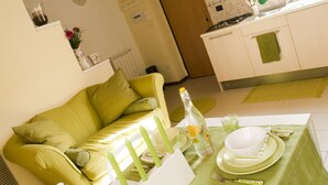 A dining area with a table set for four, a sofa, and a kitchen in the background. - Camera 40 - In Gorgonzola (Gorgonzola)