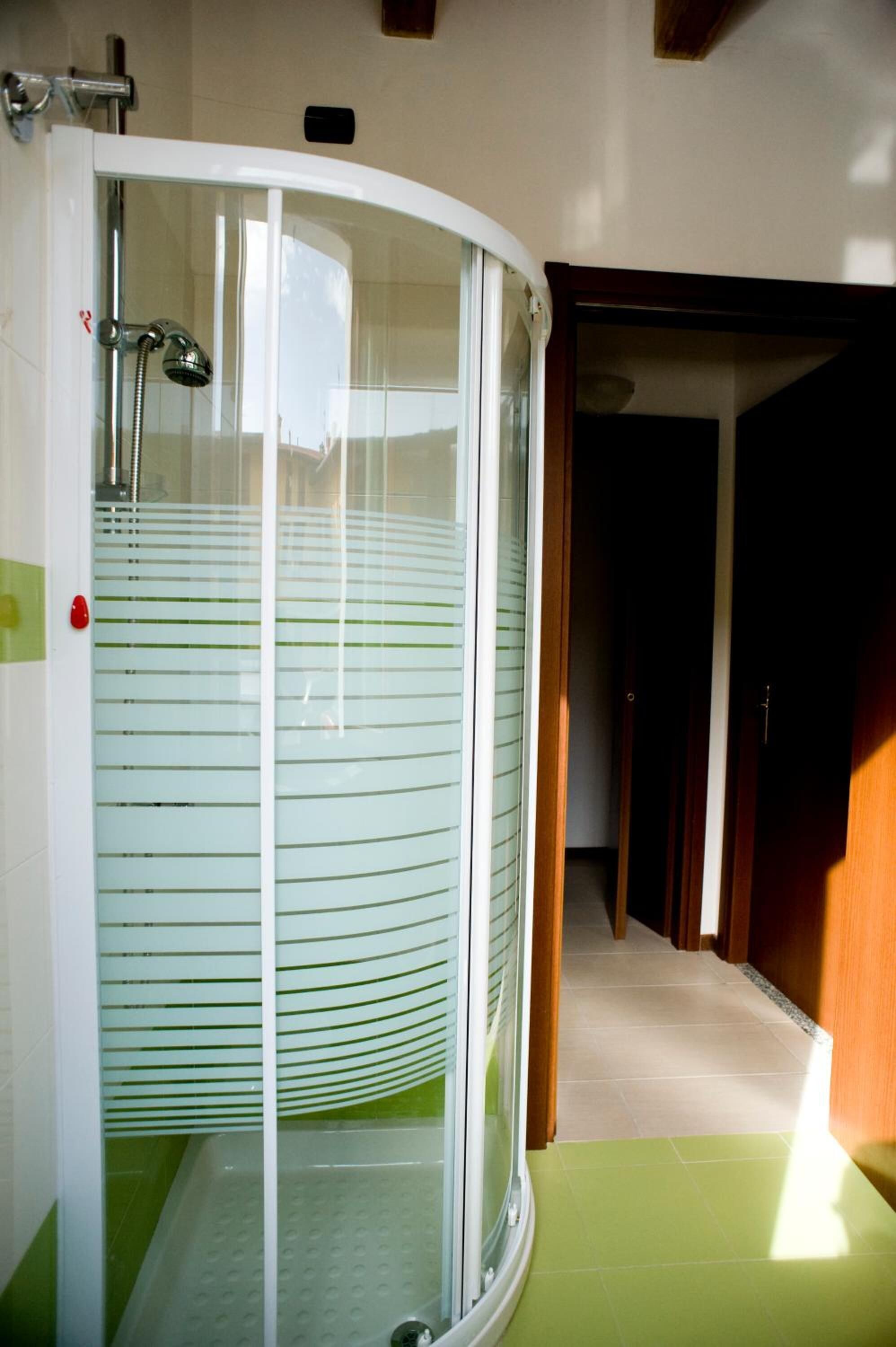 A glass-enclosed shower area with a green mat, a visible showerhead, and a tiled floor.