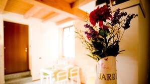 A dining area with a table and chairs, a vase with flowers, and a door in the background. - Camera 40 - In Gorgonzola (Gorgonzola)