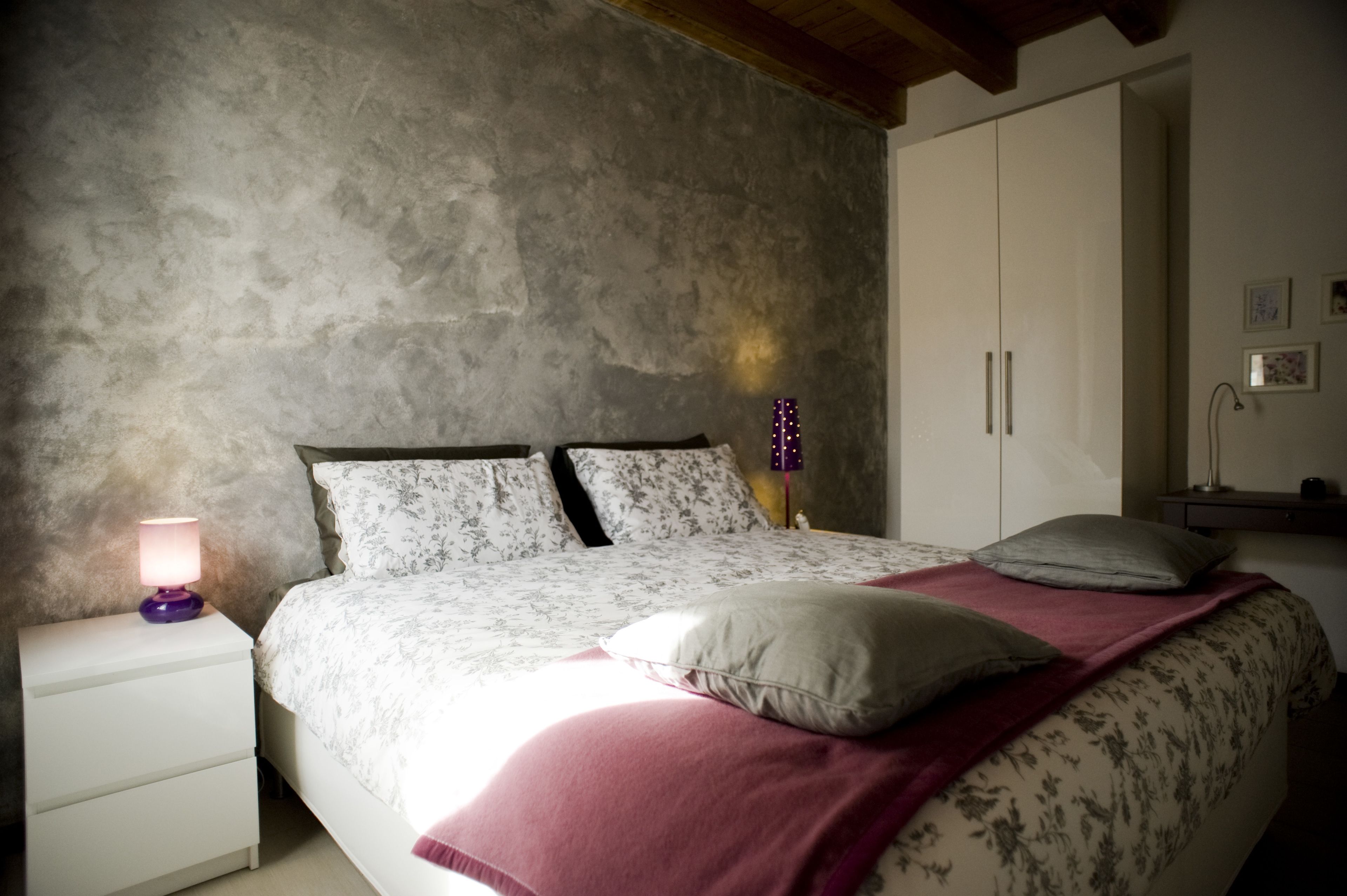 Un dormitorio con cama, mesita de noche, armario y una lámpara de pared.