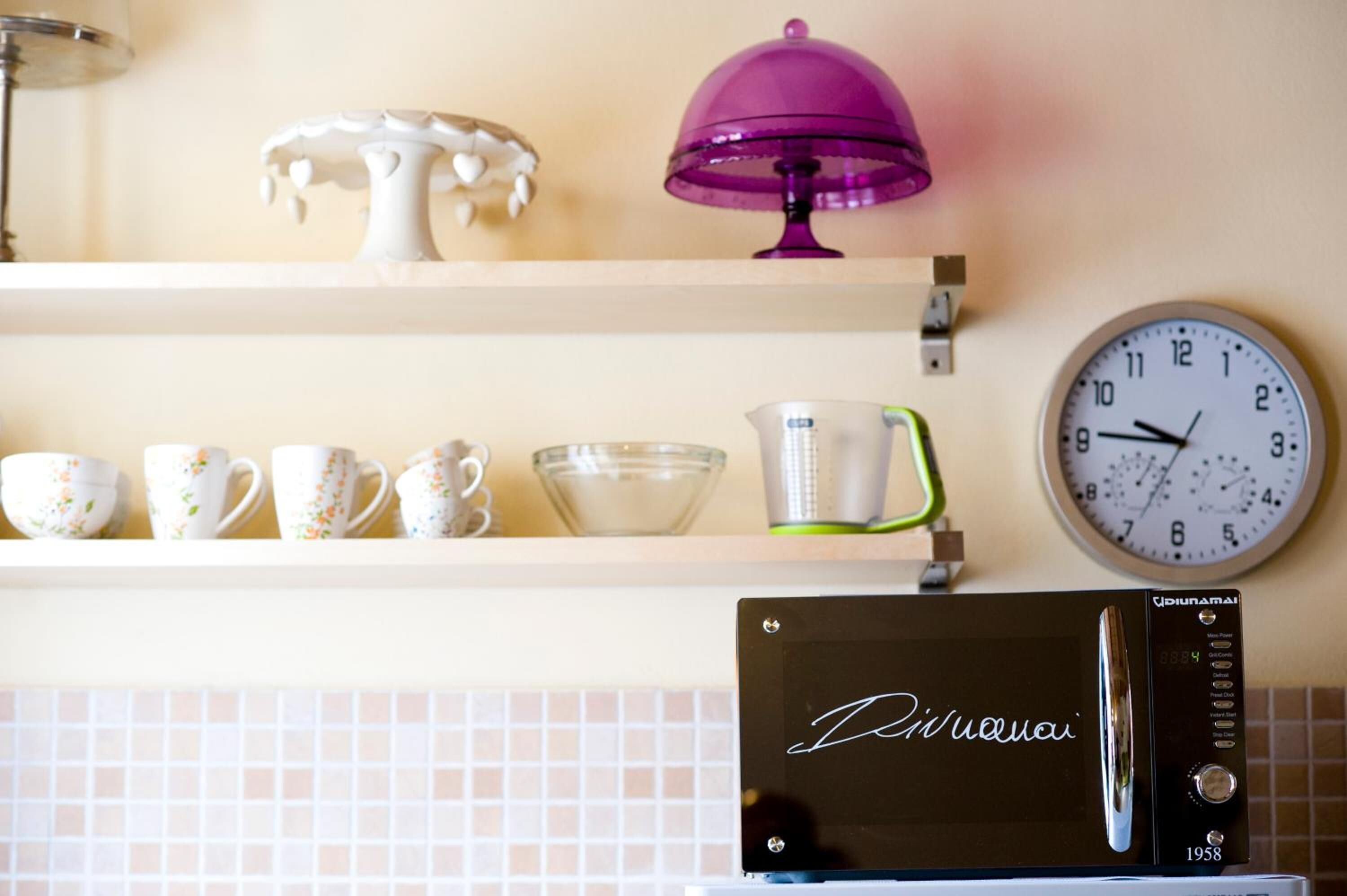 Une cuisine équipée d’un four à micro-ondes, d’une horloge et d’objets décoratifs placés sur une étagère.