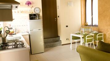 A kitchen with a refrigerator, stove, and dining area with chairs and a table.