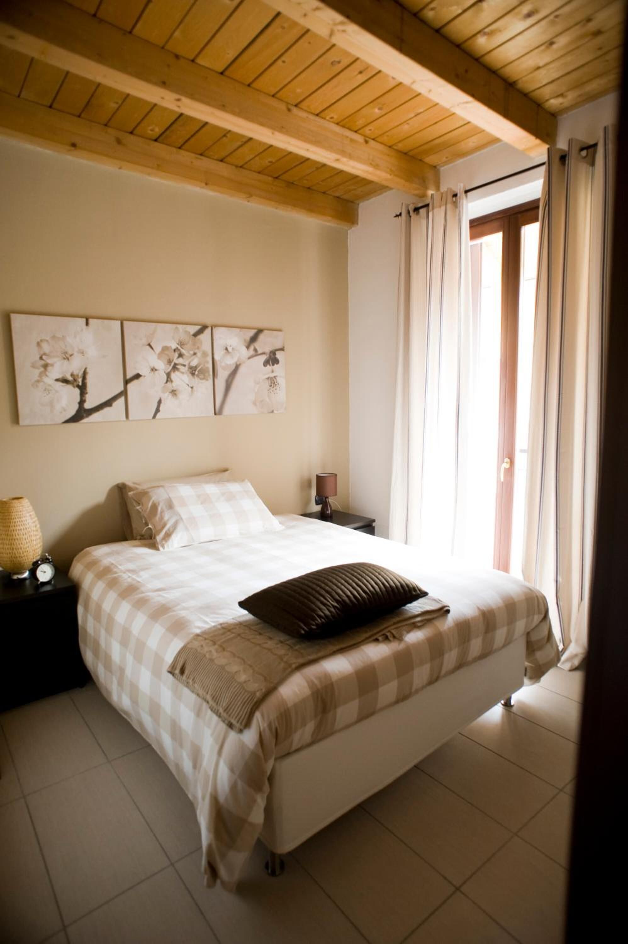 Un dormitorio con cama, mesita de noche, lámpara y un cuadro de flores en la pared.