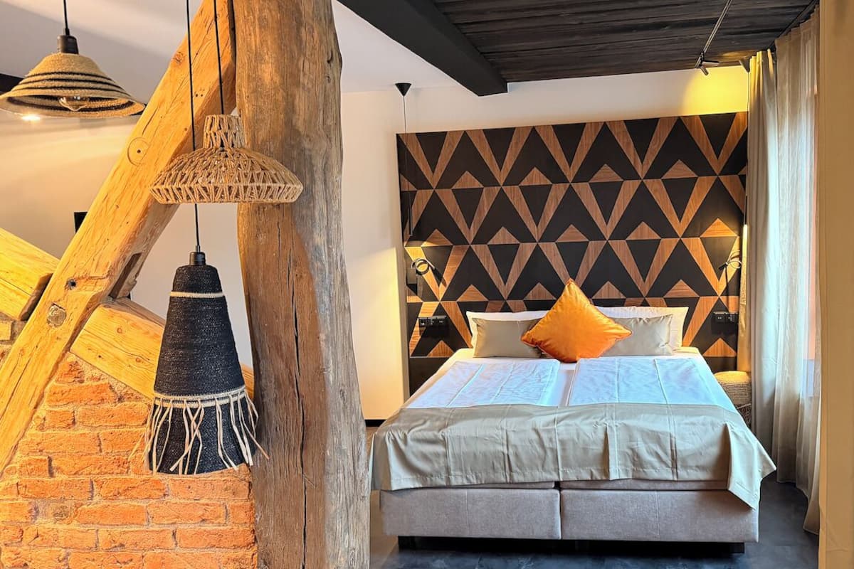 A bedroom with a bed, a geometric patterned headboard, hanging lamps, and a rustic wooden structure.