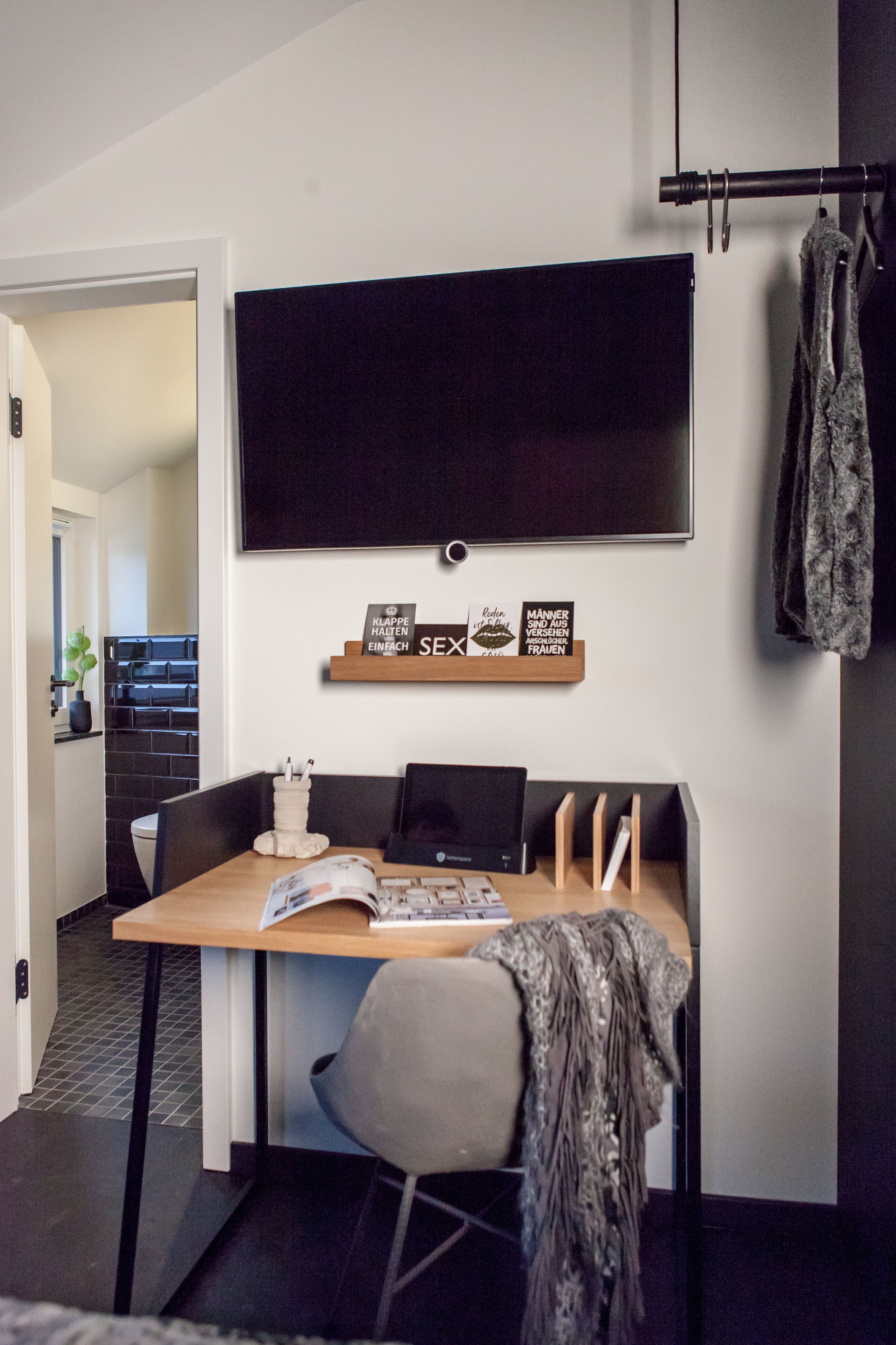 Un comedor moderno con una mesa de madera, sillas, un televisor montado en la pared y una estantería con citas inspiradoras.
