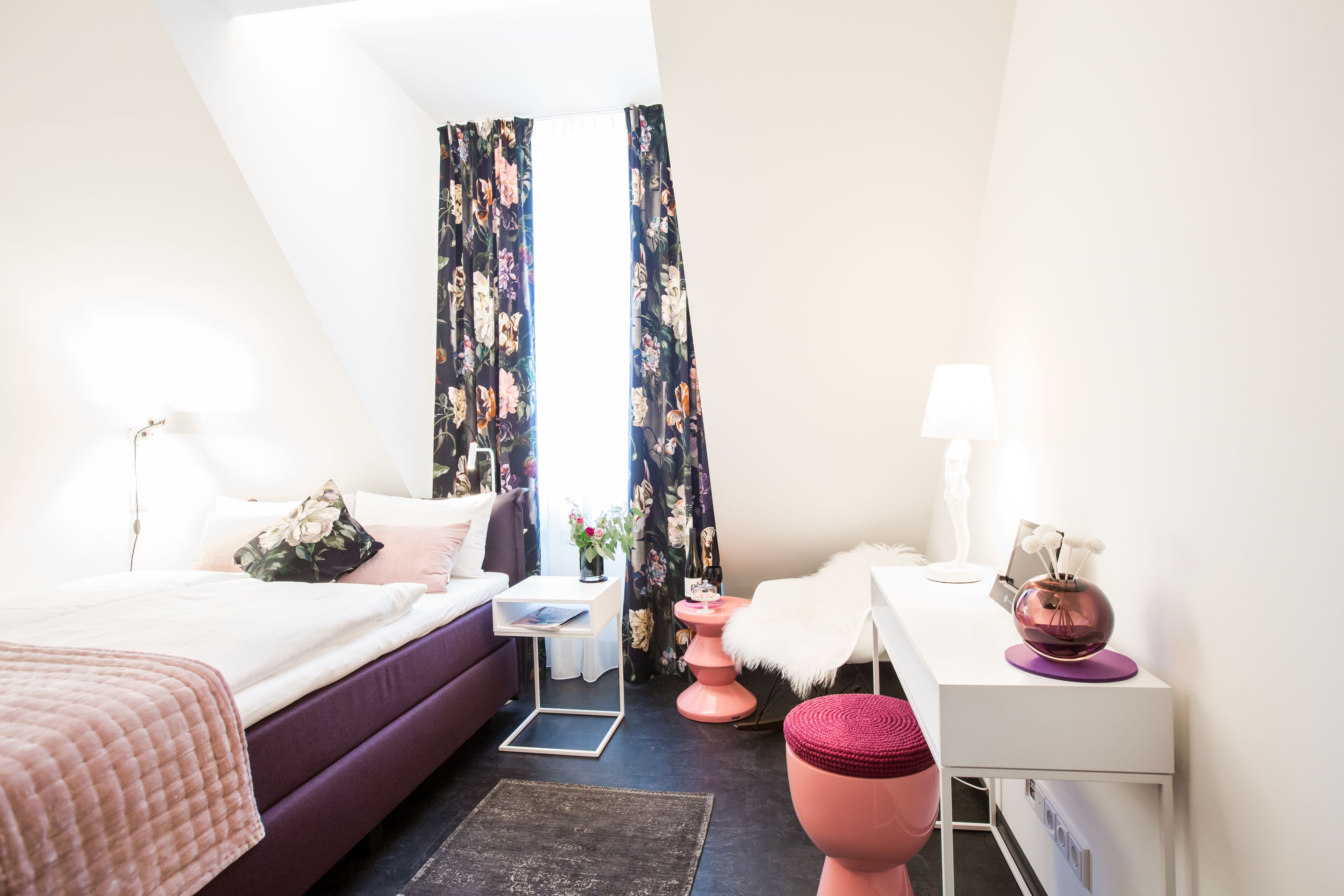 Un dormitorio moderno con cama, mesita de noche, escritorio y un pequeño taburete.