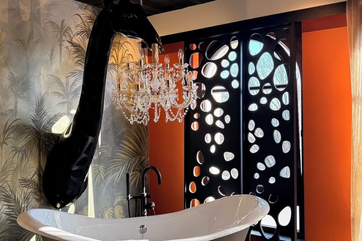 A bathroom with a freestanding bathtub, a chandelier, and a decorative wall with a tropical mural.