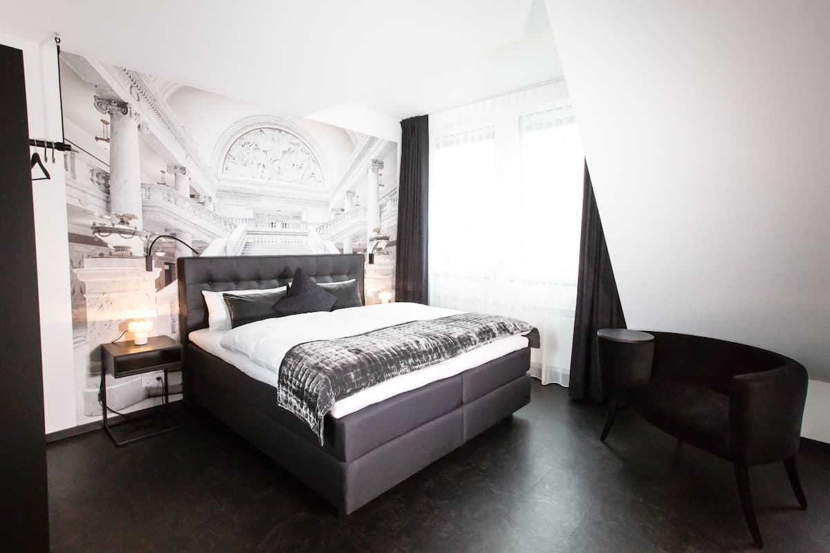 A modern bedroom with a large bed, a nightstand, a chair, and a mural on the wall.