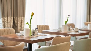 Un comedor con mesas dispuestas para dos, con vajilla blanca y un jarrón con una flor amarilla.