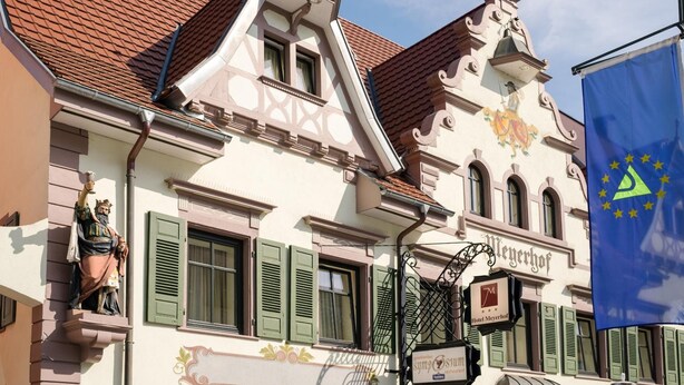 Un edificio histórico con un estilo arquitectónico europeo tradicional, que destaca una imponente torre del reloj y una bandera con el emblema de la Unión Europea.