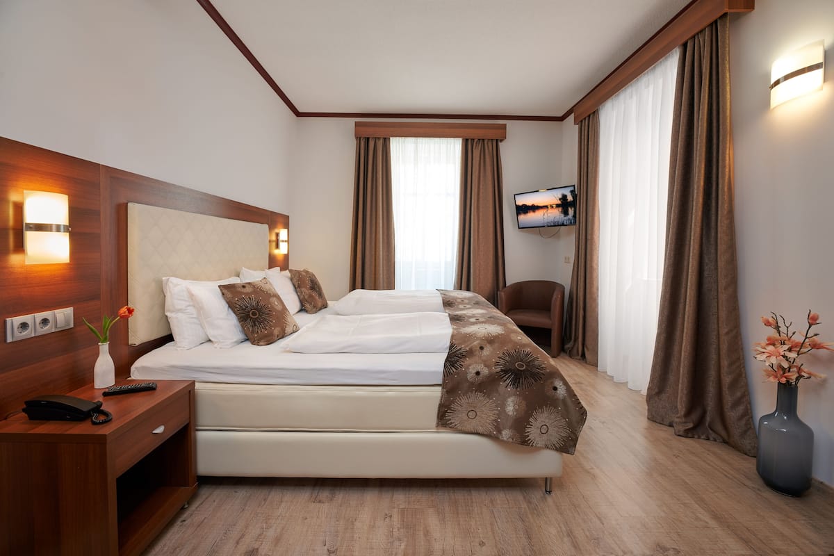 Quarto de hotel com cama, mesa de cabeceira, televisão e cortinas.