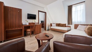 Una habitación de hotel moderna con sofá, una mesa de comedor, televisor y un ventanal con cortinas.