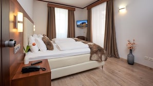 Habitación de hotel con cama, televisor montado en la pared, escritorio con control remoto y un florero con flores.
